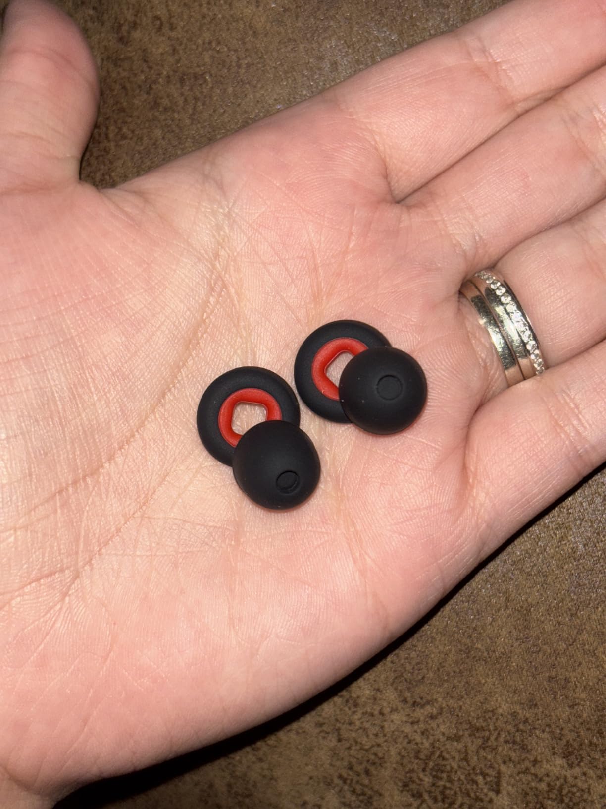 Three black and red earbud tips held in a hand on a brown surface.