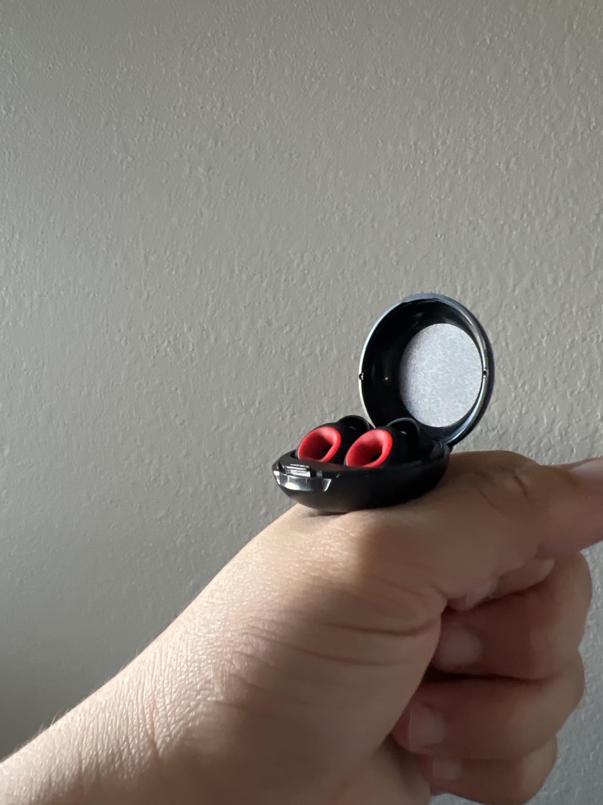 Hand holding an open black case with red earbuds against a plain background